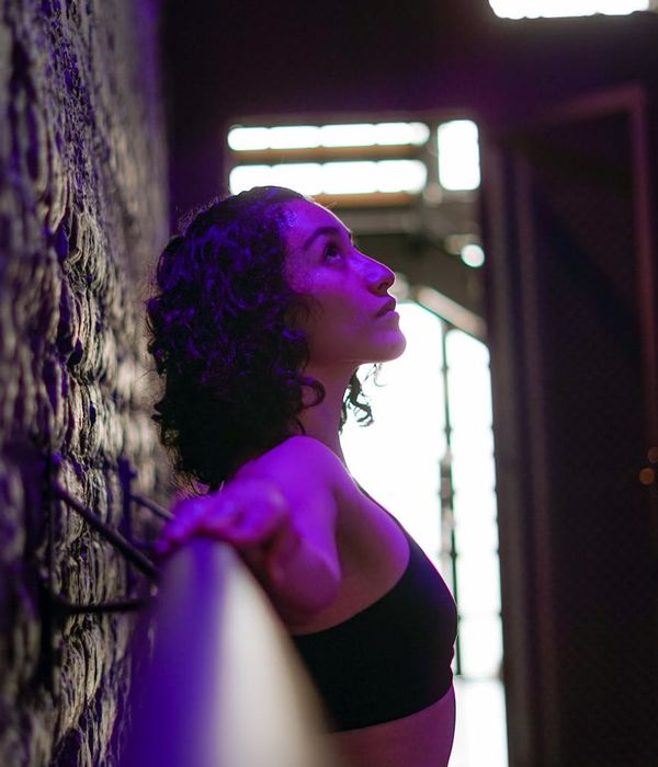 Woman in a serene yoga pose in a dark studio with purple light.